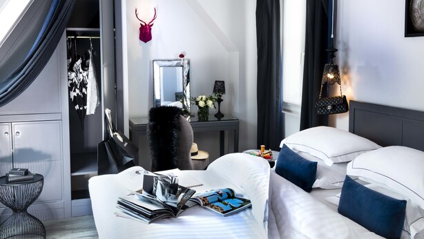 Una habitación de hotel moderna con cama, mesita de noche y un pequeño escritorio con espejo y flores.
