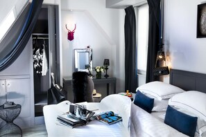 Ein modernes Hotelzimmer mit Bett, Nachttisch und einem kleinen Schreibtisch, an dem sich ein Spiegel und Blumen befinden.