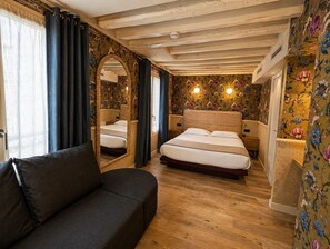 Une chambre avec un plafond en bois, un papier peint à motifs floraux, un lit double, un canapé et un miroir.