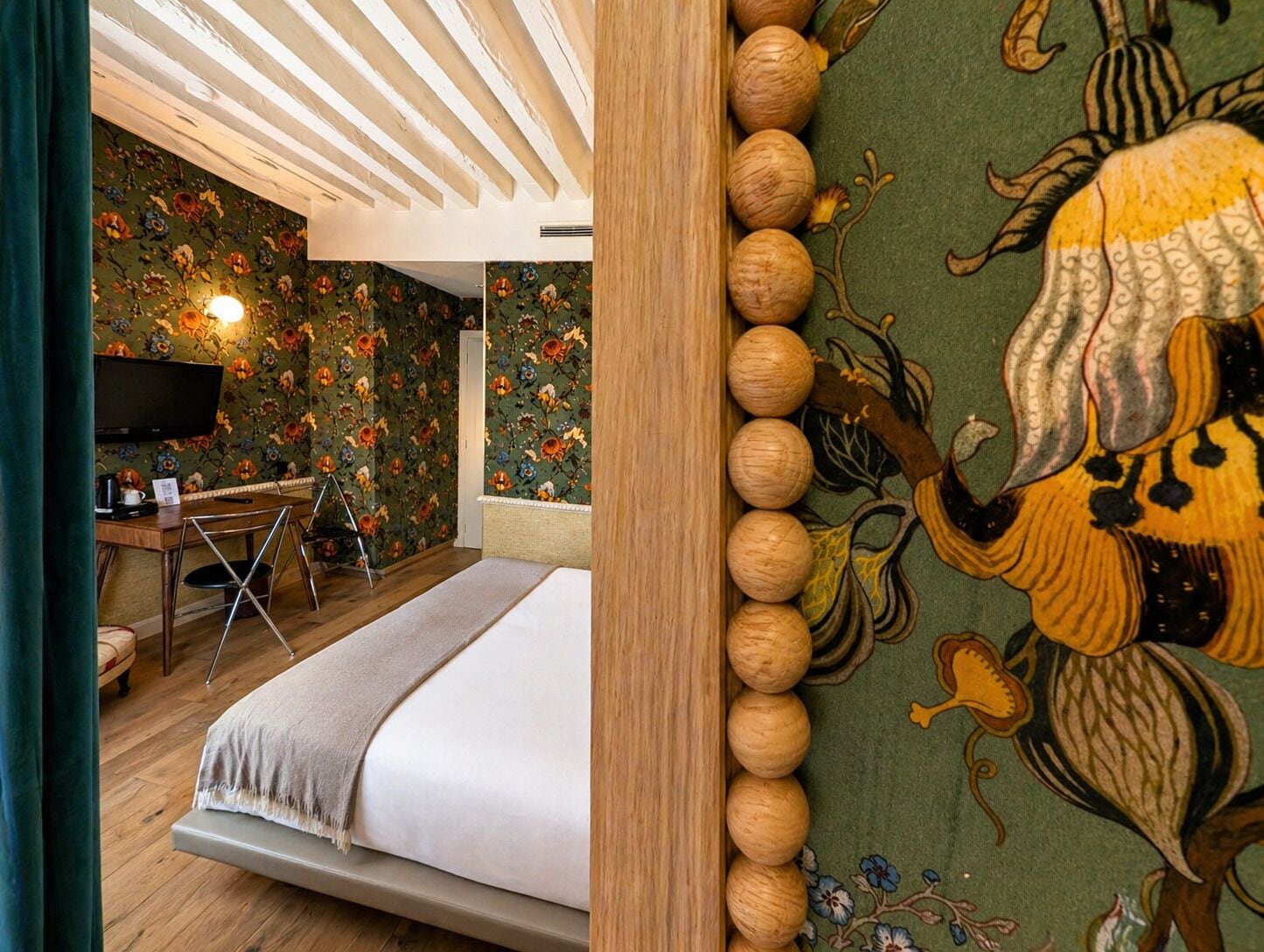 A room with a bed, a desk, a chair, a television, and a wall with a floral pattern.