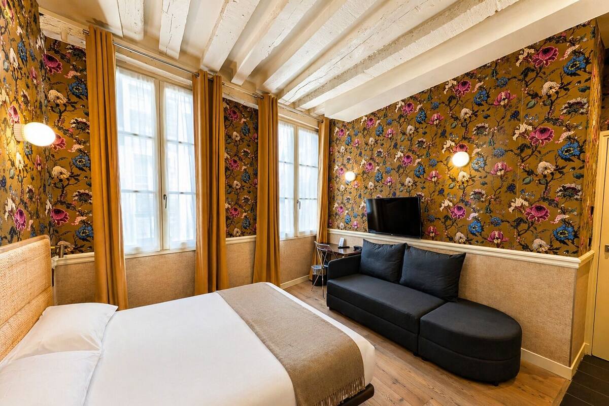 Une chambre d’hôtel avec un lit, un canapé, une télévision et un papier peint à motifs floraux.