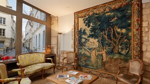 Una habitación con un gran tapiz, muebles antiguos y vistas a la calle a través de amplios ventanales.