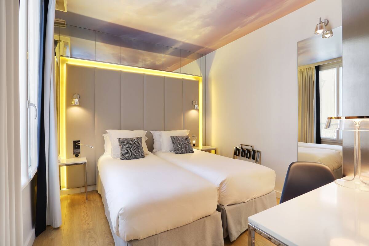 Ein modernes Hotelzimmer mit zwei Betten, einem Schreibtisch und einem Fenster mit Vorhängen.
