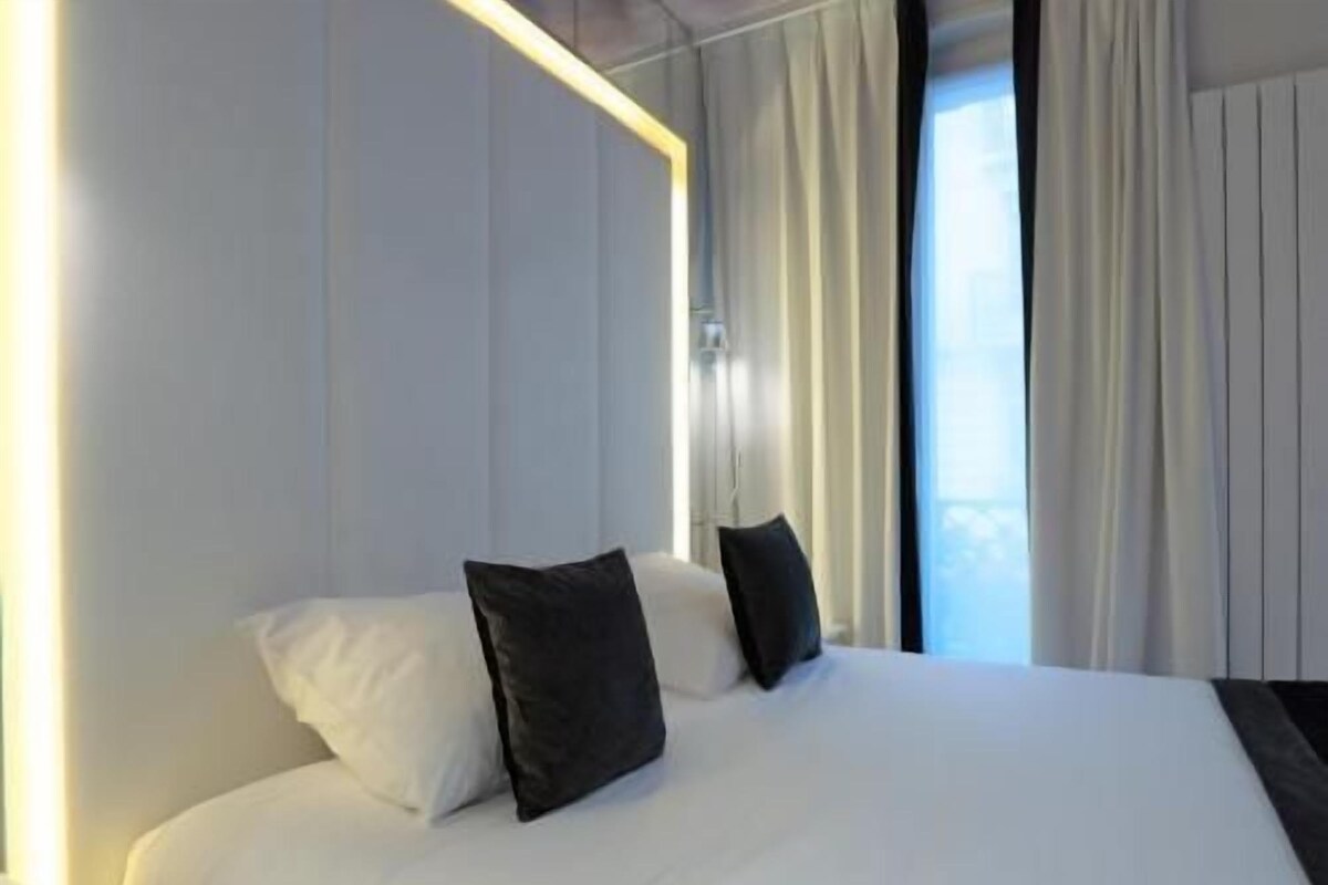 A hotel room with a large bed, a nightstand, and a window with curtains.