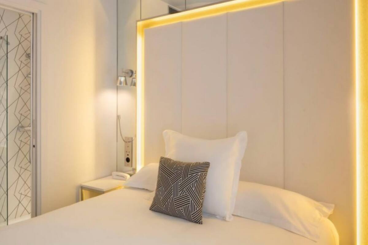 Ein modernes Hotelzimmer mit einem großen Bett, einem Nachttisch, einem Spiegel und einem Badezimmer mit Waschbecken und Duschkabine.