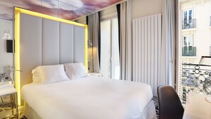 A hotel room with a large bed, a desk with a lamp, and a view of the city through the window. - Nouvel Hotel Eiffel (Paris)