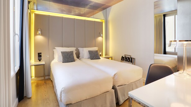 A modern hotel room with two beds, a desk, and a window with curtains. - Nouvel Hotel Eiffel (Paris)