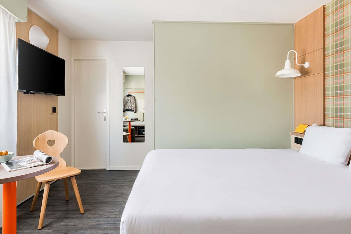 Una habitación de hotel con una cama, un escritorio con una silla, un televisor y un espejo.