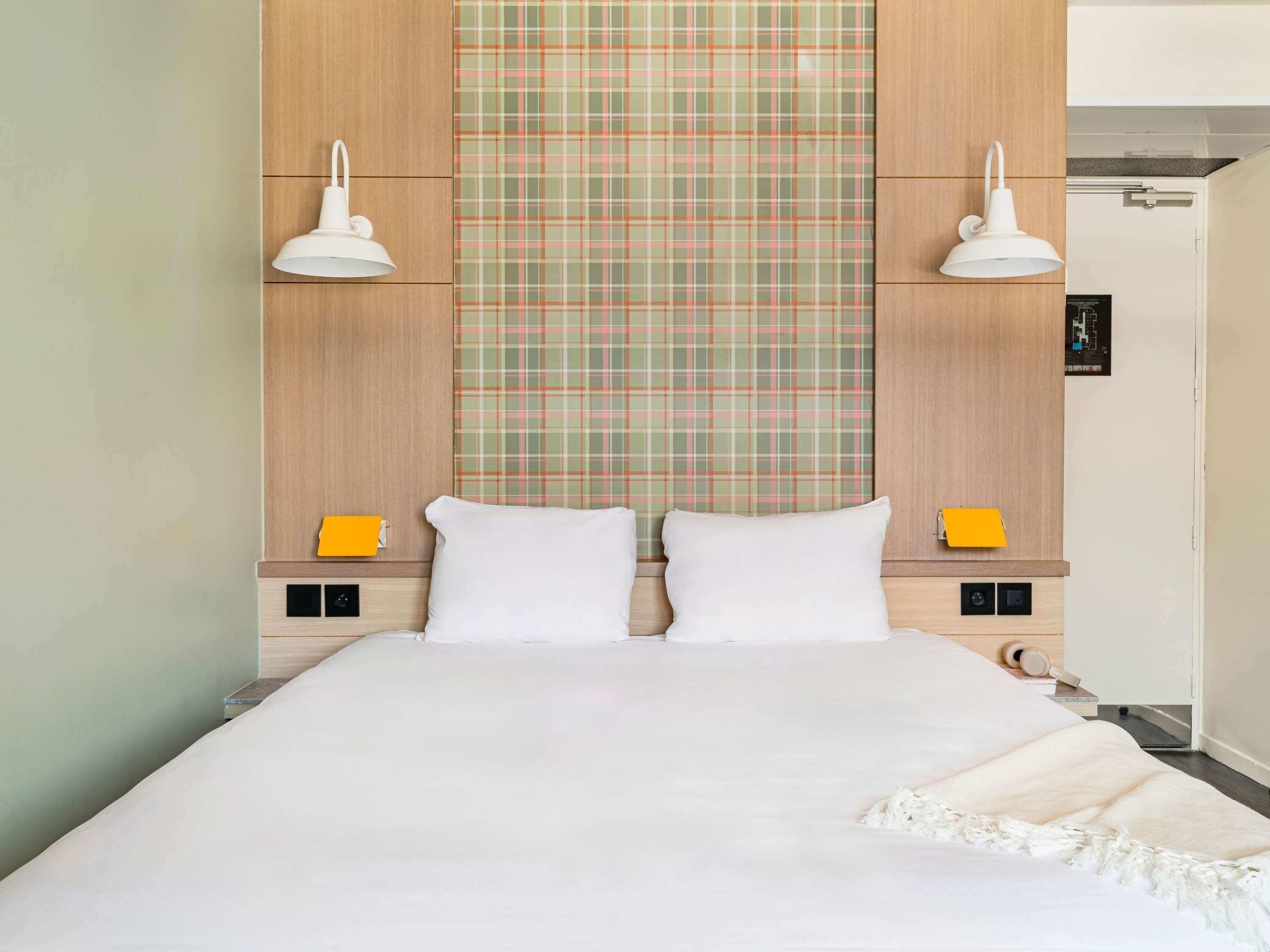 A neatly arranged hotel room with a large bed, two bedside tables, a plaid-patterned headboard, and two wall-mounted lamps.