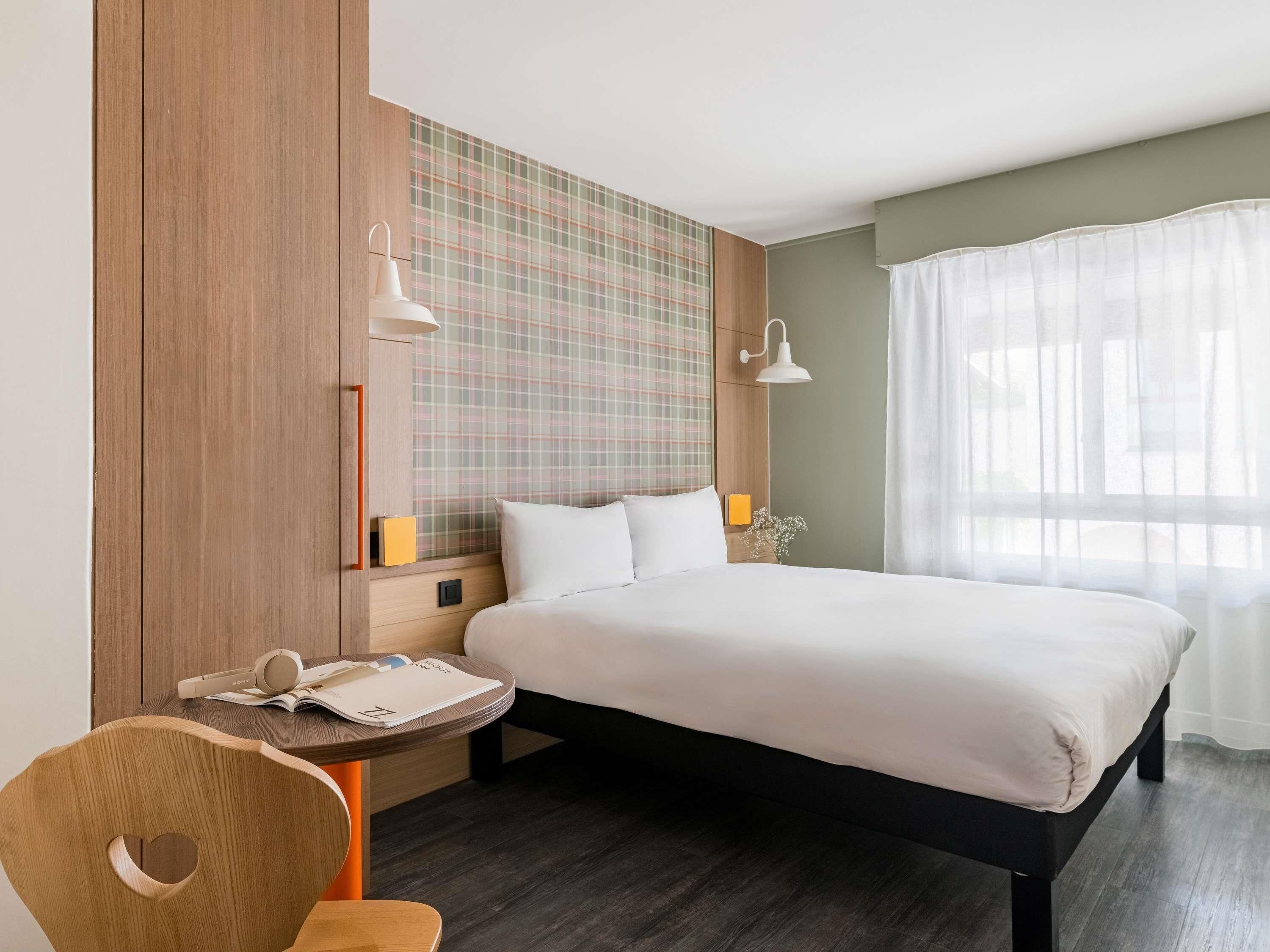 Une chambre d’hôtel comprenant un lit, des tables de chevet, un bureau, une chaise, une lampe fixée au mur et une fenêtre avec des rideaux.