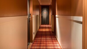 Un pasillo de hotel con piso alfombrado, puertas a ambos lados y un letrero con número en la pared.