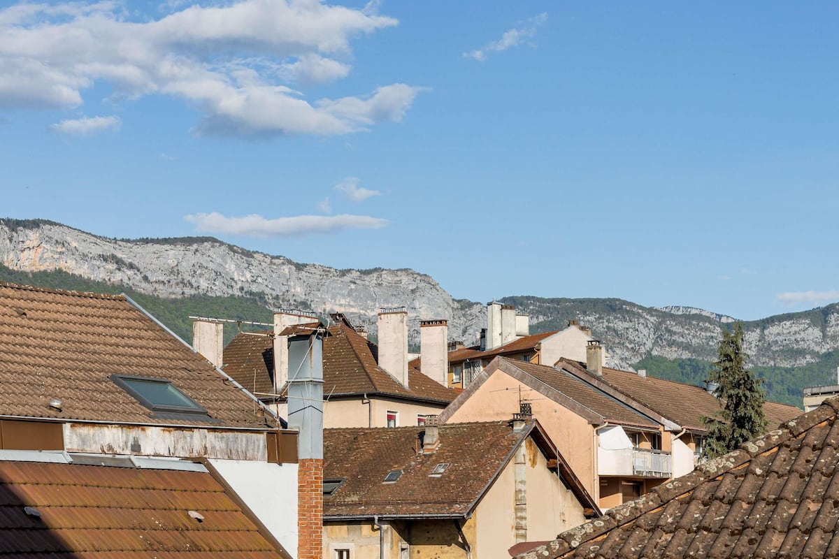 Zona residencial con tejados de tejas rojizas, montañas al fondo y cielo despejado.