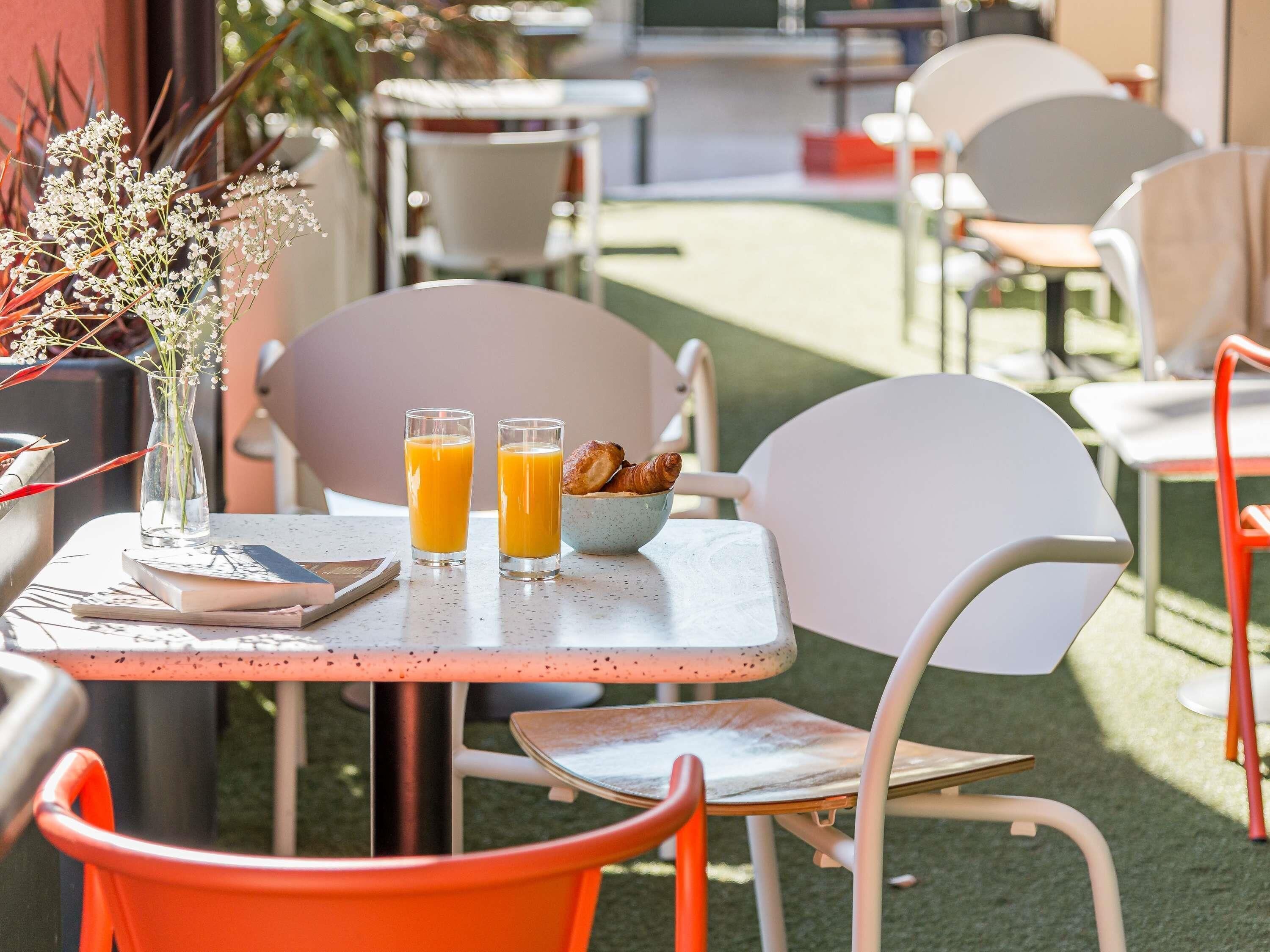 An outdoor cafe with a table, chairs, a vase with flowers, and two glasses of orange juice.