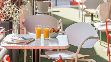 An outdoor cafe with a table, chairs, a vase with flowers, and two glasses of orange juice.