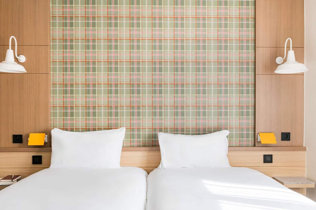 Habitación de hotel con dos camas, papel tapiz escocés, lámparas de noche y una mesita de noche con un libro.