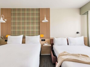 Een hotelkamer met twee bedden, een hoofdbord met ruitpatroon, bedlampjes, een nachtkastje en een kleine tafel.