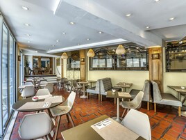 A restaurant with multiple tables and chairs, a brick floor, and a view of the street.