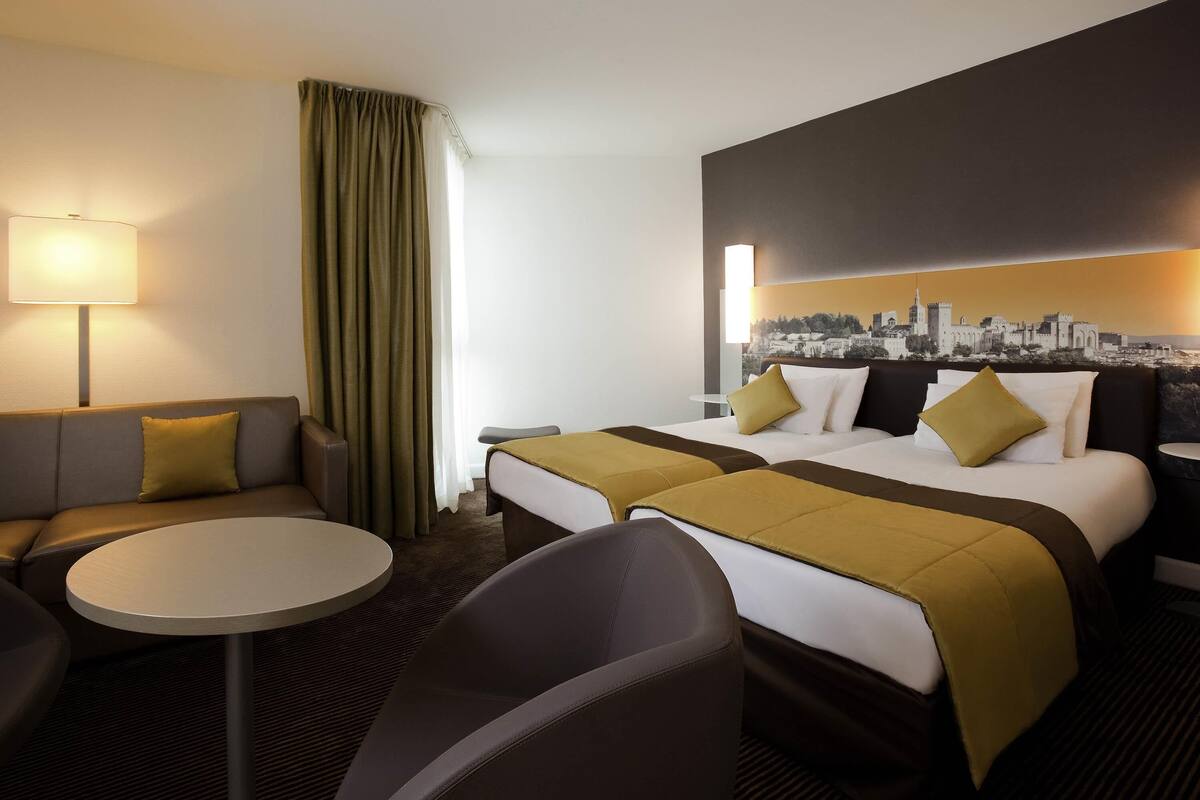 Una habitación de hotel con cama, dos mesitas de noche, sofá, una mesa redonda y una lámpara.