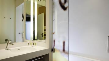A modern bathroom with a glass shower enclosure, a white sink, and a large mirror.