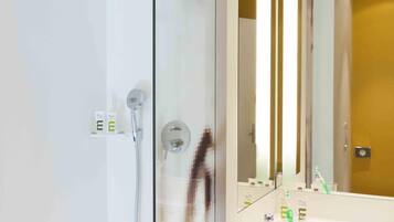 A modern bathroom with a glass shower enclosure, a large mirror, and a white sink with toiletries.