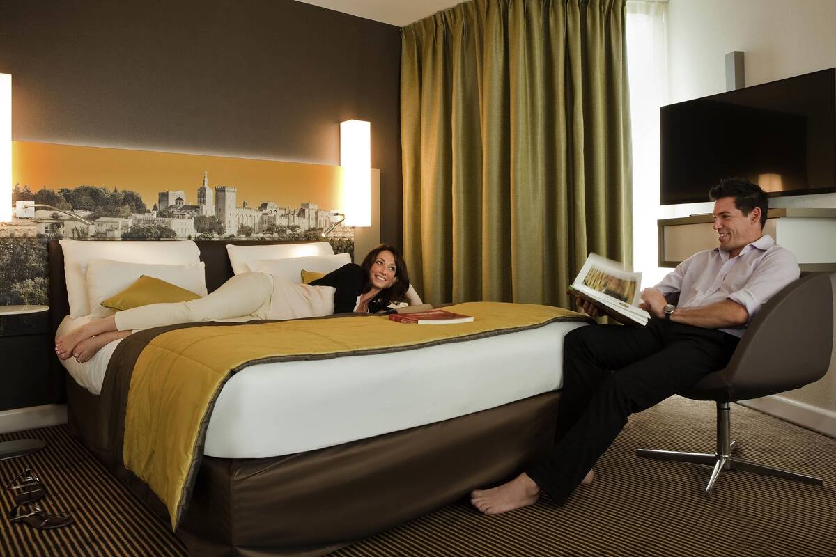Habitación de hotel con cama, un mural de paisaje urbano, televisor y ventana con cortinas.