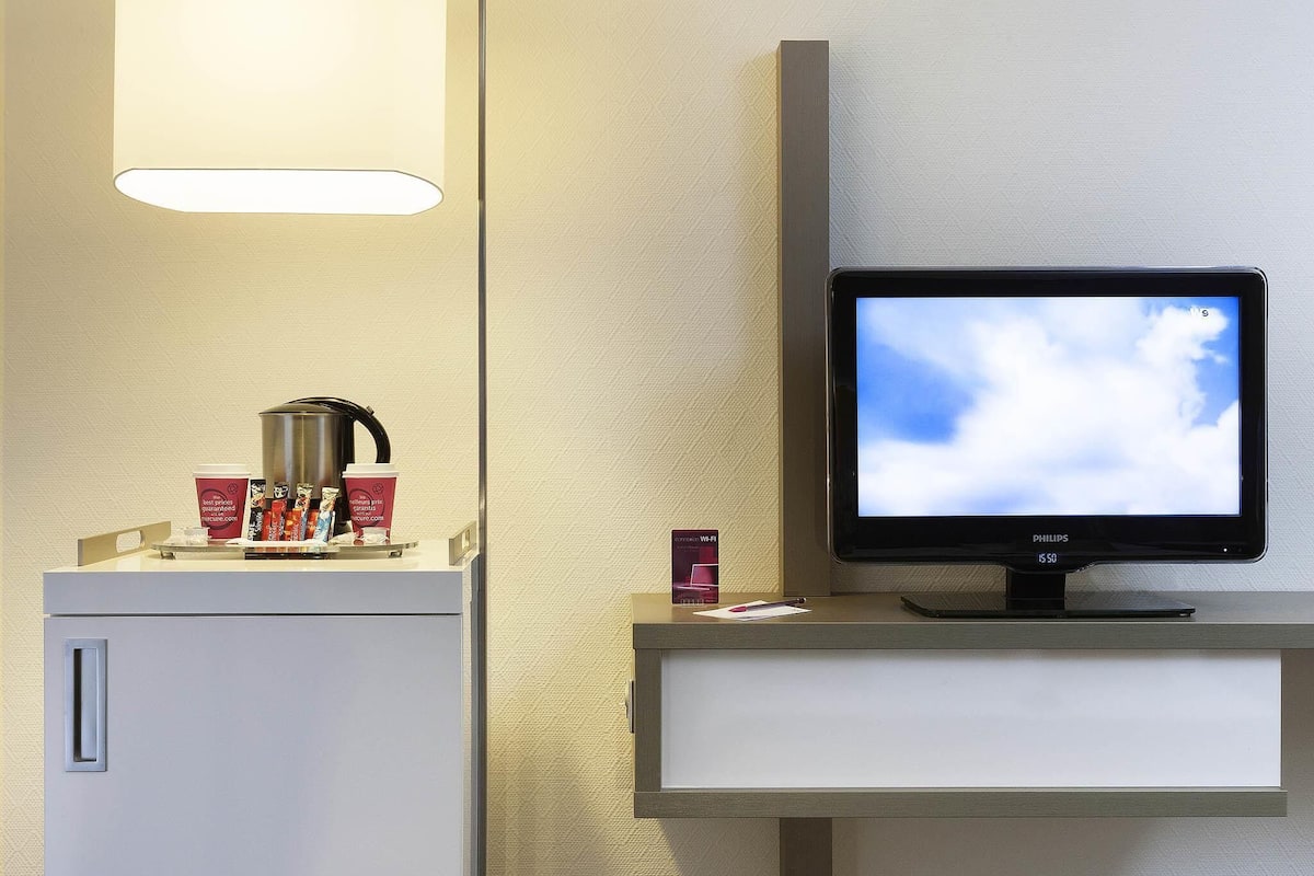 Ein Hotelzimmer mit Flachbildfernseher, Kaffeemaschine und einer Kaffeetasse auf einer Ablagefläche.