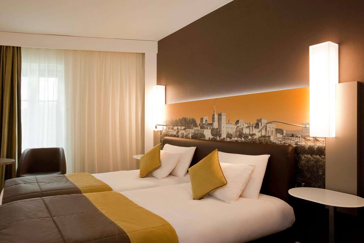 Una habitación de hotel con dos camas, un mural de paisaje urbano en la pared y una mesa redonda.