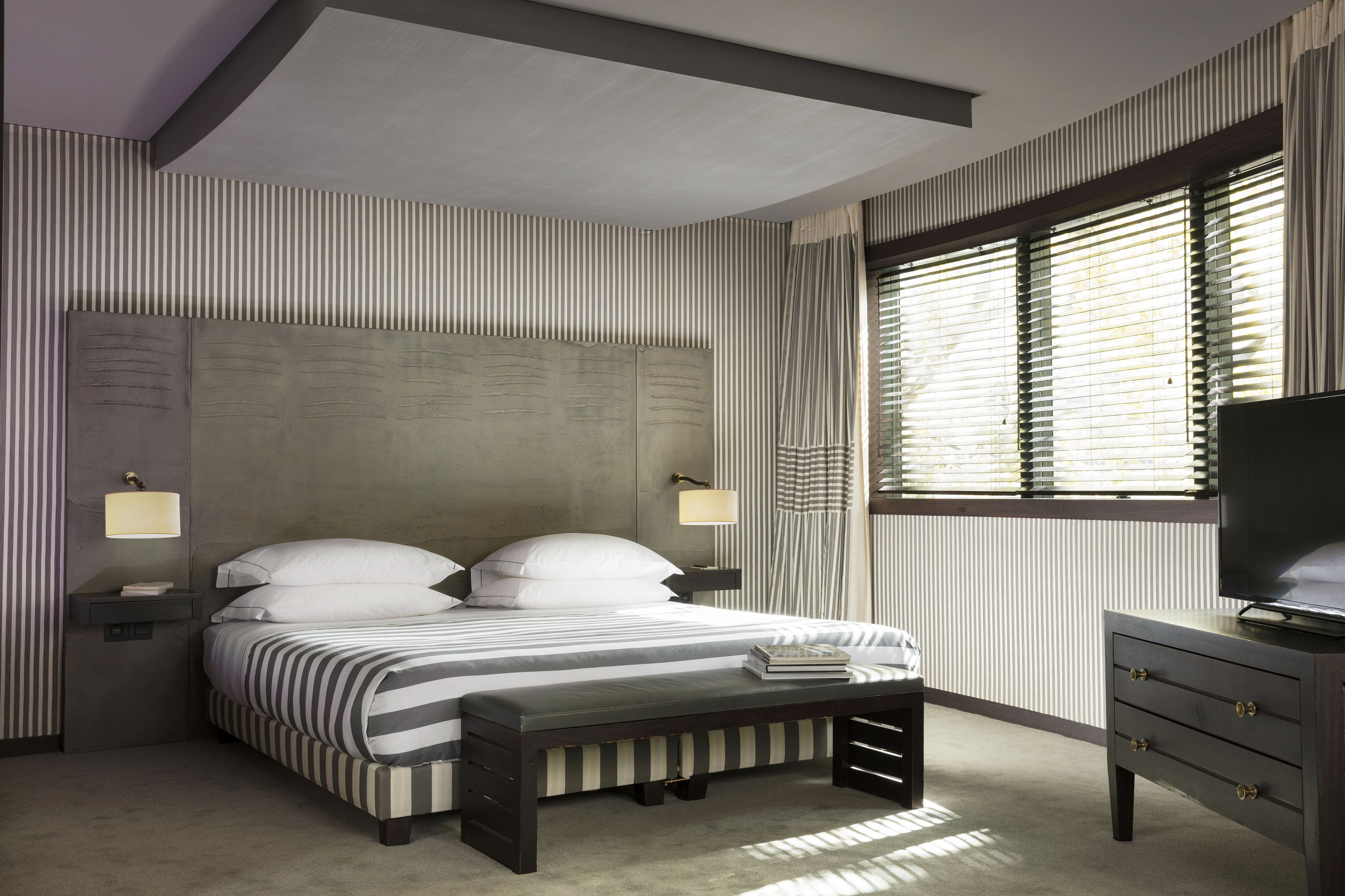 A modern bedroom with a large bed, bedside lamps, a bench, and a TV on a dresser.