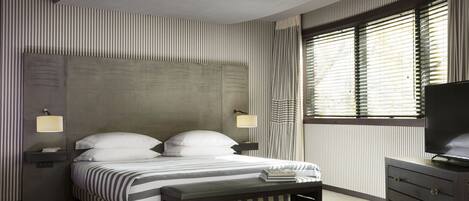 A modern bedroom with a large bed, bedside lamps, a bench, and a TV on a dresser.