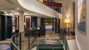 Um hall de hotel moderno com uma escadaria em espiral, um balcão de recepção e uma grande pintura abstrata na parede.