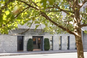 Entrada de hotel con fachada de piedra, puertas dobles y un pequeño vestíbulo con un banco.