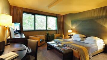 A hotel room with a bed, desk, chairs, and a TV.