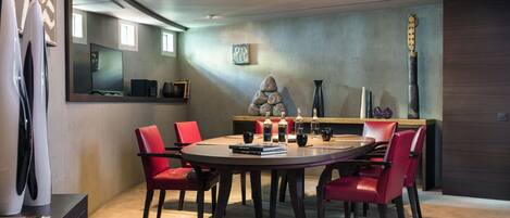 Un comedor moderno con una mesa redonda, sillas rojas y una escultura de piedra.