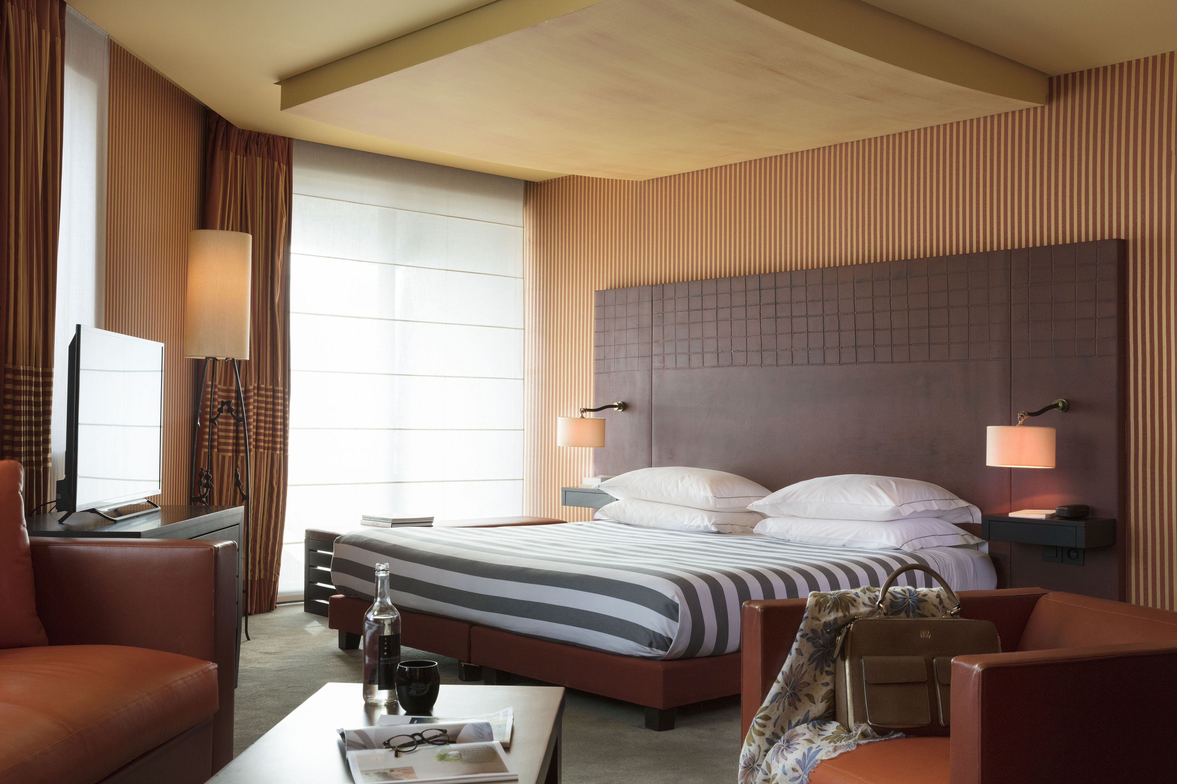 A hotel room with a large bed, a desk with a lamp, a sofa, and a television.
