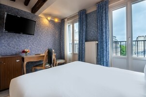 Camera d'albergo con un letto grande, una scrivania con una sedia, una TV a schermo piatto montata a parete e vista sulla città da ampie finestre.