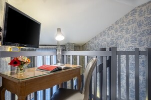 A room with a wooden desk, a TV, a lamp, a chair, and a decorative vase with flowers.