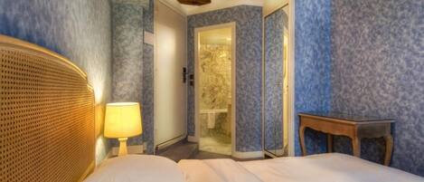 Habitación de hotel con cama, mesita de noche, lámpara, cabecero de madera, espejo y puerta que da a un baño.