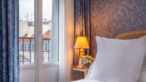 Una habitación de hotel con cama, mesita de noche con lámpara y ventana con cortinas.