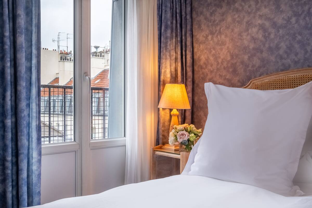 A hotel room with a bed, a nightstand with a lamp, and a window with curtains.