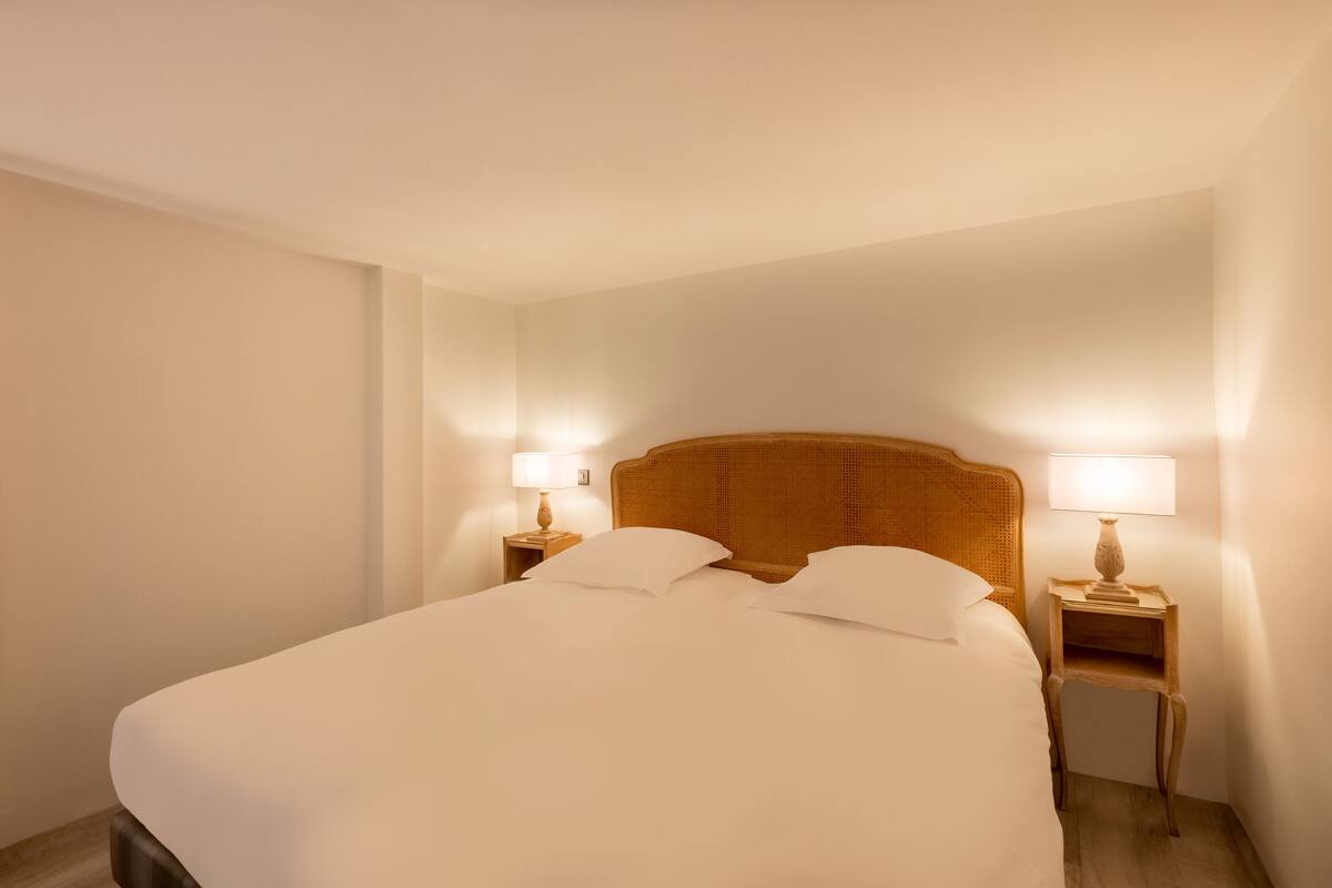 A neatly made bed with white linens and two bedside tables with lamps.