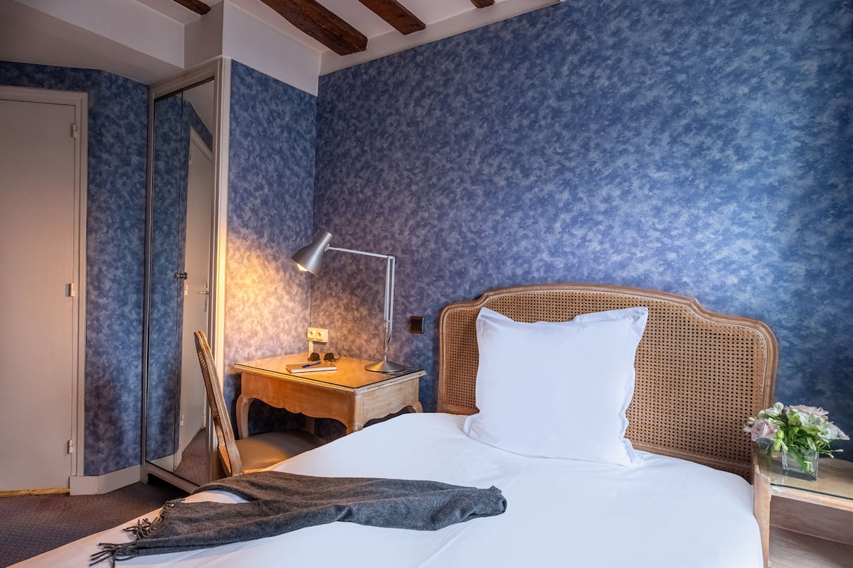 A bedroom with a bed, a nightstand, a lamp, a wooden chair, and a door.