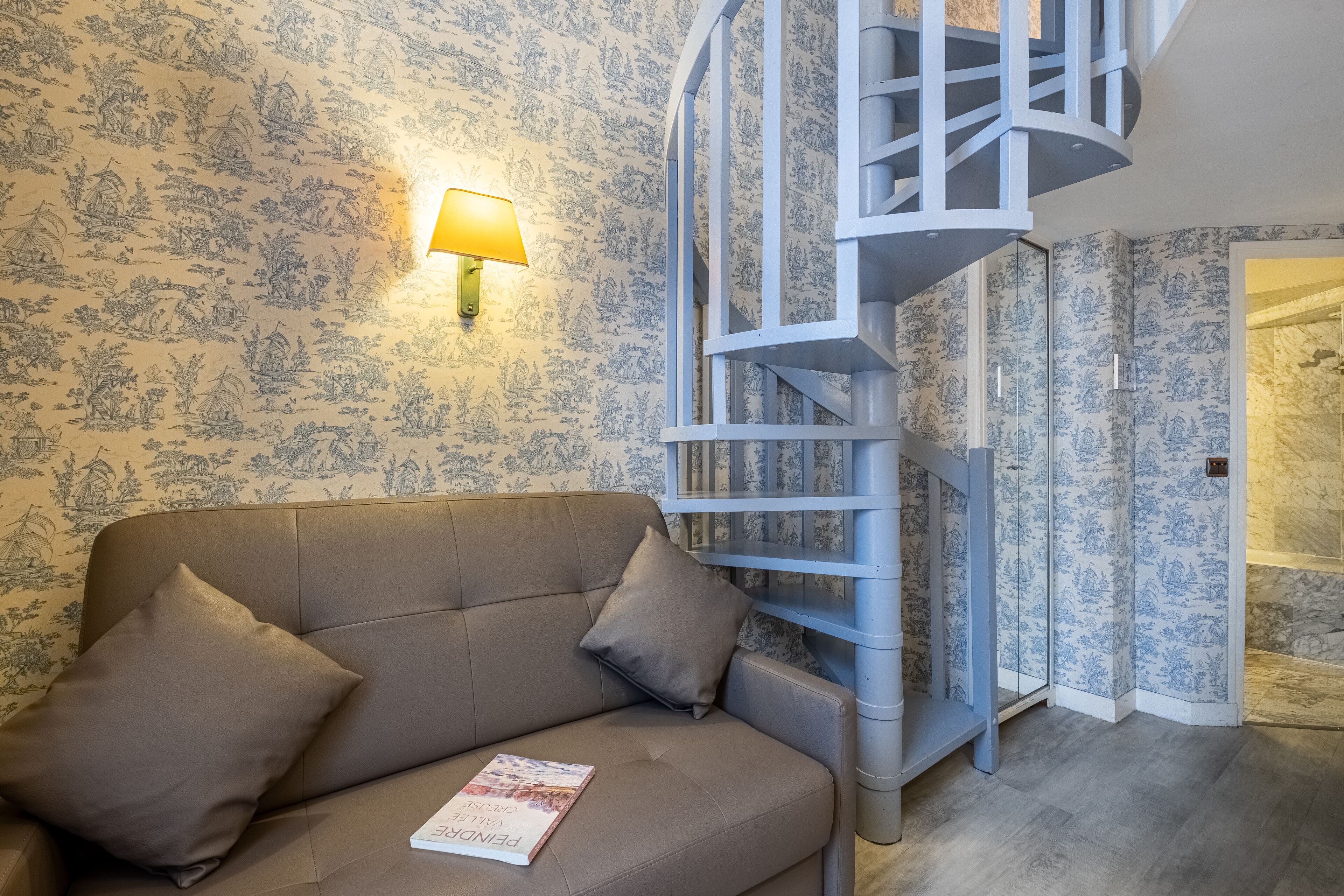 Een kamer met een beige bank, een lamp en blauw behang met een patroon.