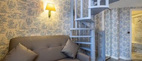 A room with a beige sofa, a lamp, and a blue patterned wallpaper.