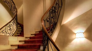Una gran escalera con barandales negros ornamentados y peldaños alfombrados de rojo.