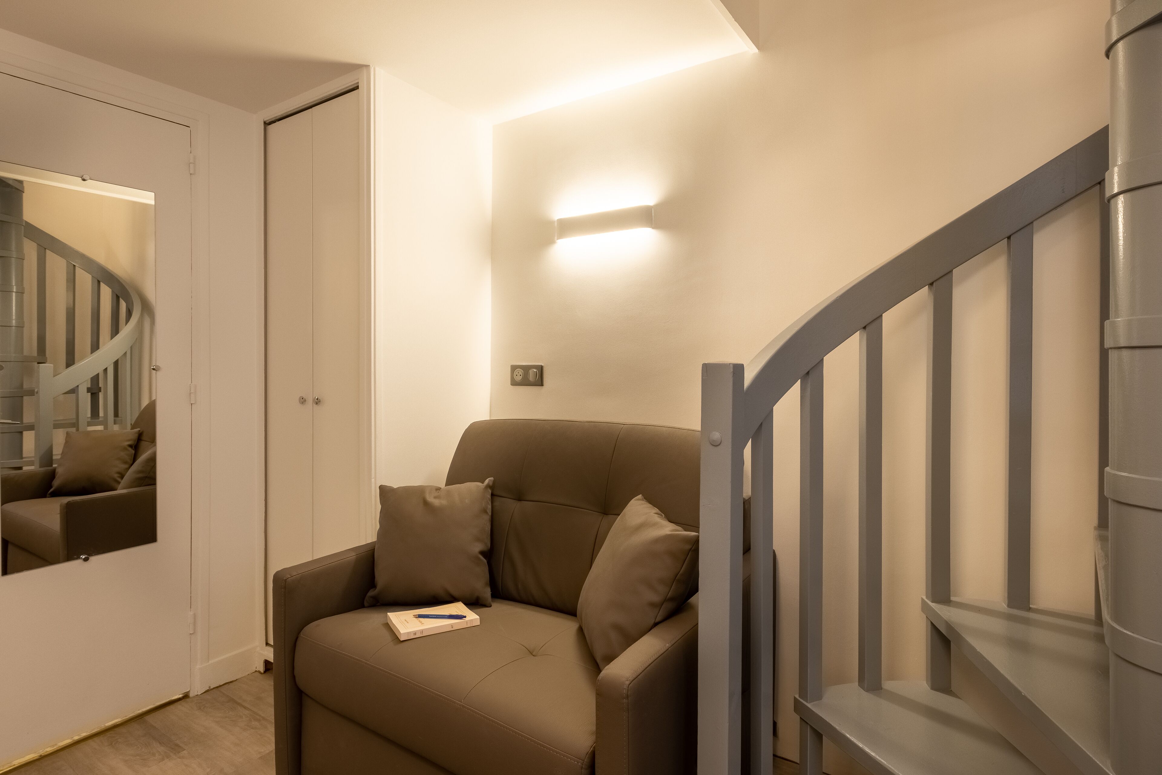 A modern living room with a sofa, a mirror, and a staircase.