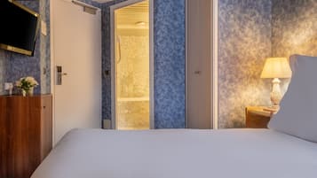 Un dormitorio con cama, cómoda de madera, televisor montado en la pared y baño a la vista a través de una puerta abierta.
