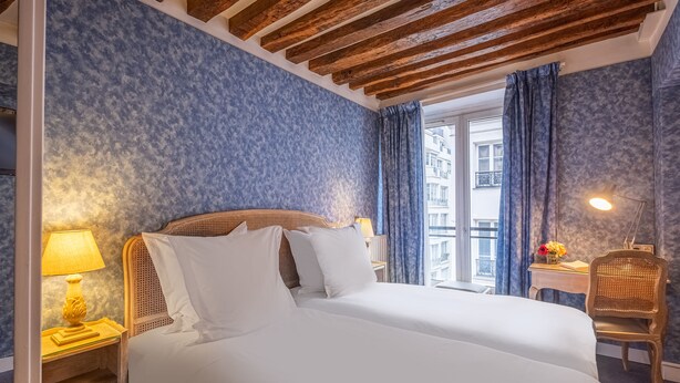 Habitación de hotel con cama, mesita de noche con lámpara, una silla y ventana con cortinas.