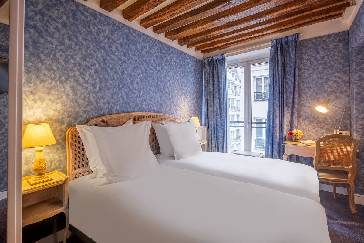 A hotel room with a bed, a nightstand with a lamp, a chair, and a window with curtains.