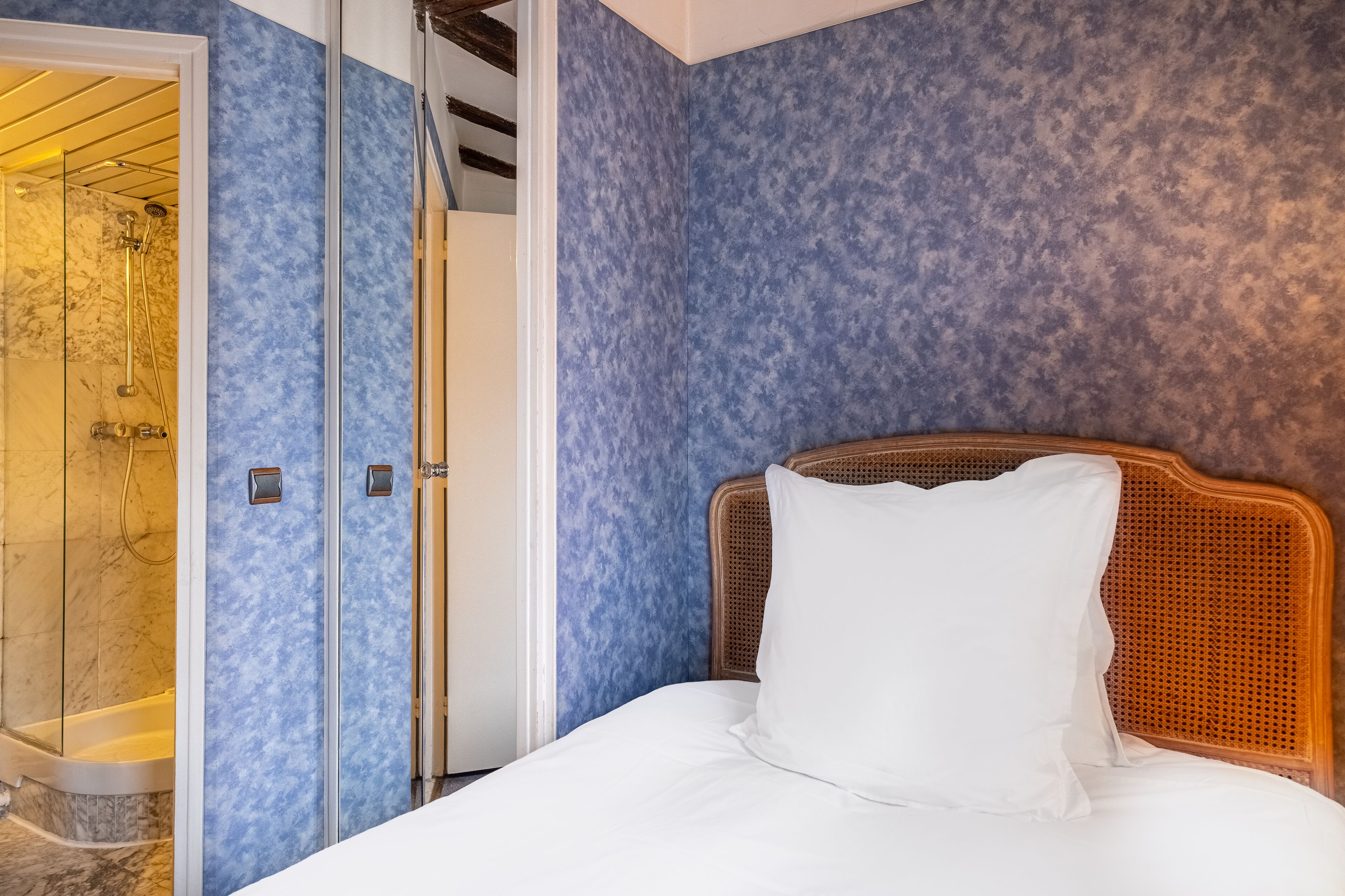 Quarto de hotel com cama, área de chuveiro e parede azul com textura.