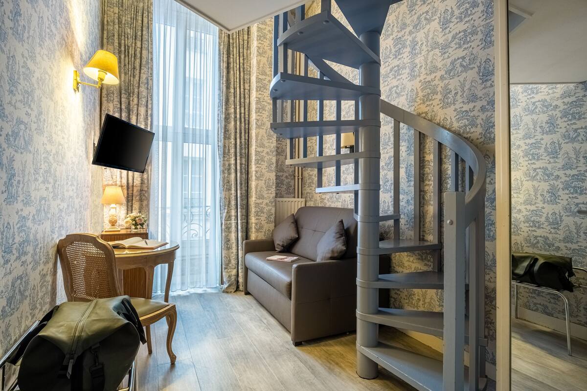 A room with a spiral staircase, a sofa, a desk with a lamp, and a chair.
